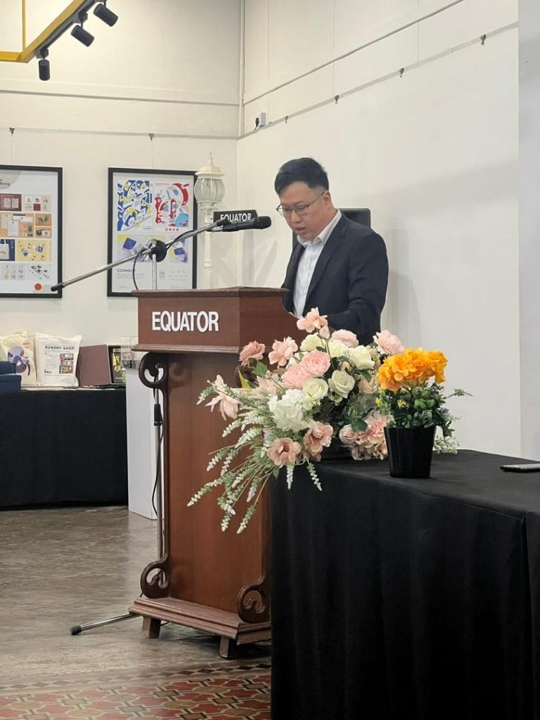 Man speaking at "EQUATOR" podium with flower arrangements.